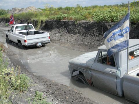 1989 Ford Bronco - Two pickup trucks navigate a muddy track, one displaying a Chevrolet flag.
