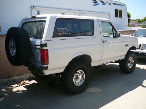 1988 Ford Bronco - This white Ford Bronco is parked outdoors next to a recreational vehicle, with a spare tire mounted on the rear.
