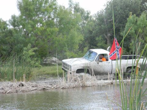1989 Ford Bronco - A white pickup truck navigates through a muddy, watery terrain, flying a Confederate flag.