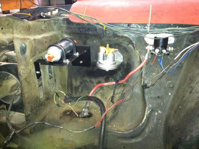 Engine bay wiring in progress with electric fuel pump, filter, and solenoid mounted on inner fender of red vehicle