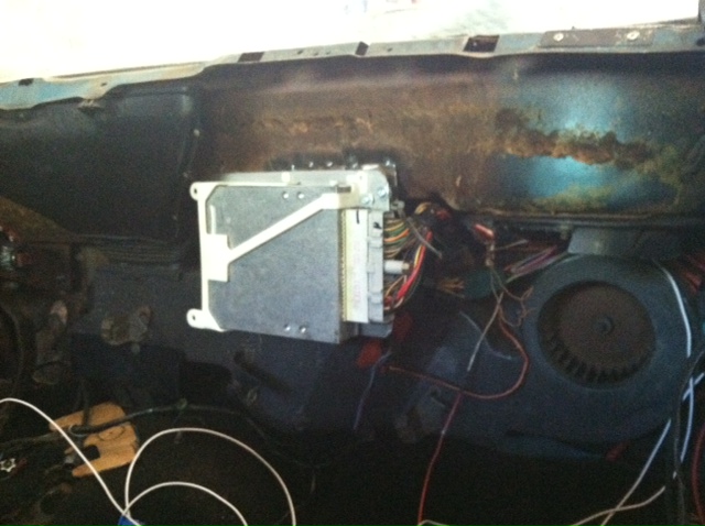 Bare firewall with electronic module on bracket, exposed wiring, and heater blower fan during restoration