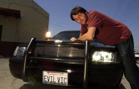 2003 Ford Crown Victoria - man rests on the hood of a black Ford Crown Victoria with brush guard, plate reads EVIL VIC