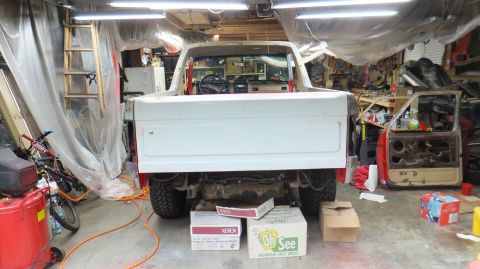 1983 Ford Bronco - A white Ford Bronco is seen from the rear in a cluttered garage, with parts and tools scattered around.