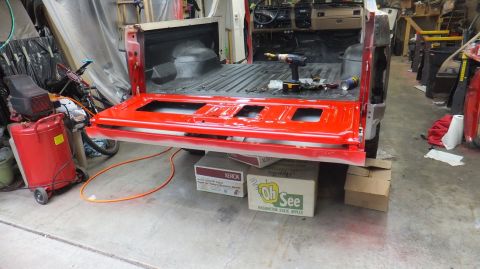 1983 Ford Bronco - The red tailgate and truck bed interior of a vehicle are visible, with tools laid out and the vehicle supported by boxes.