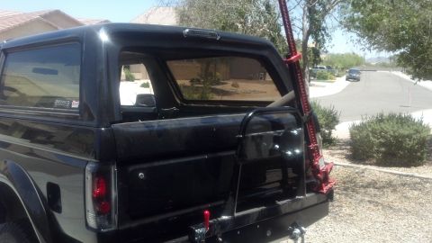 1995 Ford Bronco - This black SUV has a spare tire carrier and a Hi-Lift jack attached to the rear. A 'BRONCO' sticker is visible on the window.