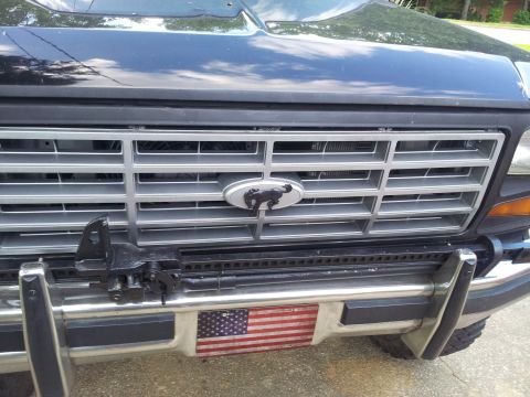 1986 Ford Bronco - The grille features horizontal bars and a horse emblem, with an American flag decal on the lower bumper.