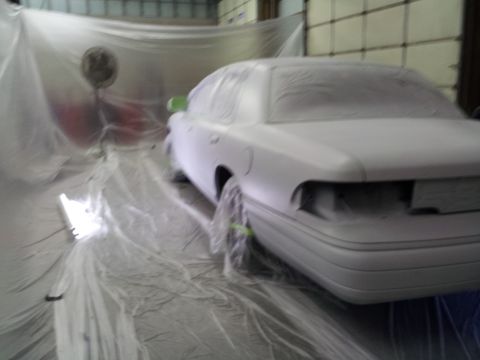 1994 Mercury Grand Marquis - Car body is covered in plastic sheeting, likely for paint preparation in a booth.