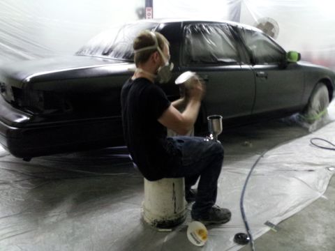 1994 Mercury Grand Marquis - A person is spray painting a car that is covered in plastic sheeting in a workshop.