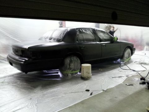 1994 Mercury Grand Marquis - A black sedan is being prepped for painting inside a booth, with plastic sheeting covering most of the vehicle.