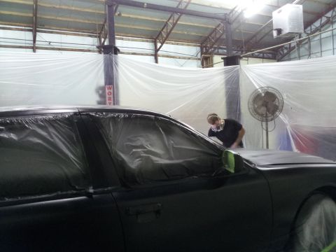 1994 Mercury Grand Marquis - A person in a mask works on a car that is covered in plastic sheeting, likely preparing it for painting.