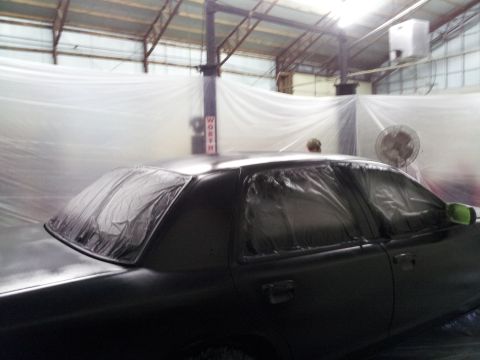 1994 Mercury Grand Marquis - A car is being prepped for painting inside a booth, with plastic sheeting covering the windows and body panels.