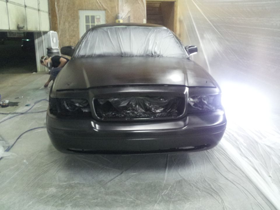 Front view of dark sedan covered in plastic, undergoing paint work