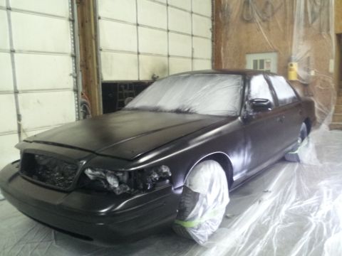 1994 Mercury Grand Marquis - A sedan is covered in plastic sheeting and plastic bags on the wheels, ready for a paint job in a workshop.