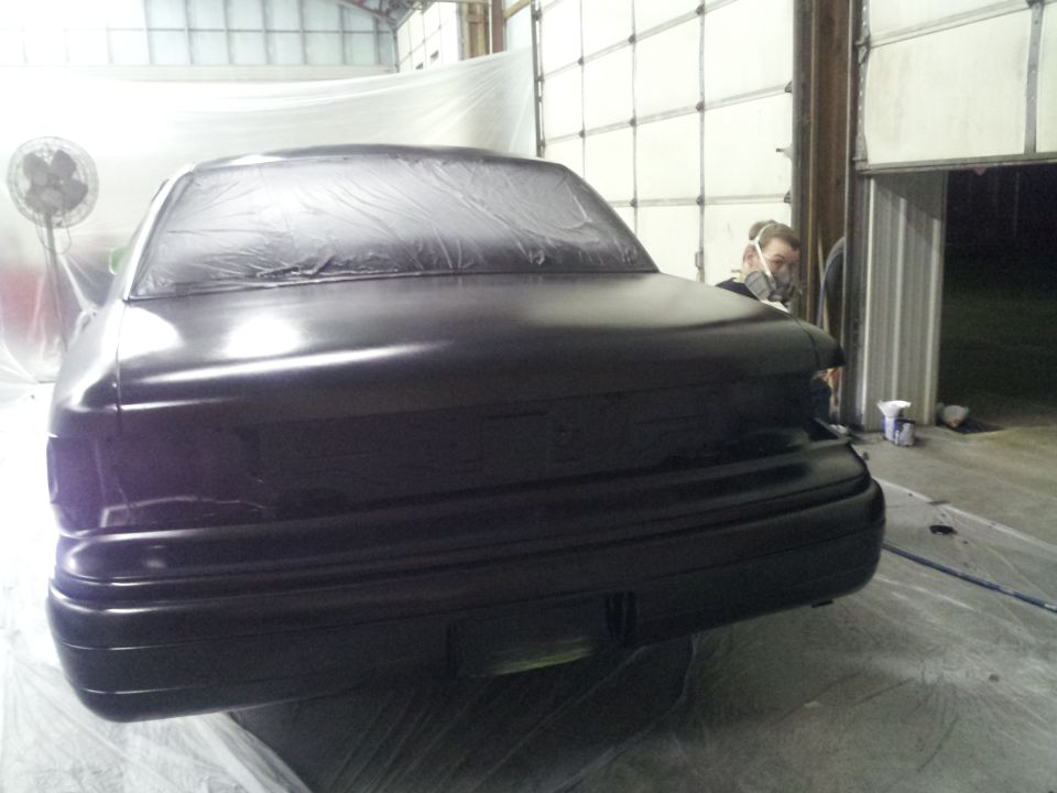 Rear view of black sedan covered in plastic, undergoing paintwork in a garage
