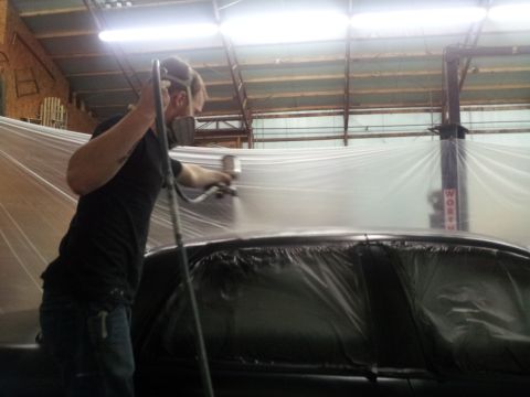1994 Mercury Grand Marquis - A person is spray painting a car that is covered in plastic sheeting inside a garage.