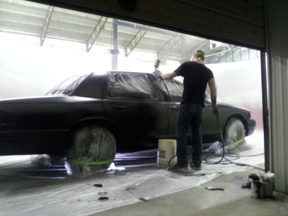 Side view of black sedan being painted in a spray booth