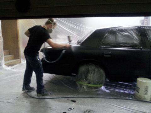 1994 Mercury Grand Marquis - A person is spray painting a car that is covered in plastic sheeting in a garage.