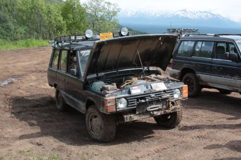2005 Jeep TJ - A black SUV sits on a dirt track with its hood open, revealing the engine compartment. Another SUV is visible behind it.