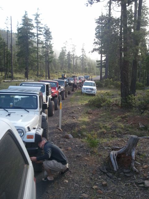 1994 Ford Bronco - A convoy of off-road vehicles travels down a wooded dirt path, with one person attending to a tire.