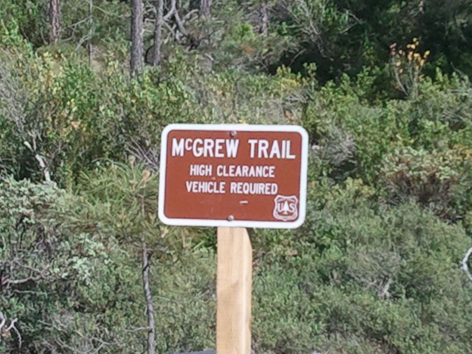 Sign for McGrew Trail, says high clearance vehicle required. Forested background