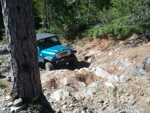 1994 Ford Bronco - Jeep Wrangler tackling a difficult, rocky trail in a wooded area.