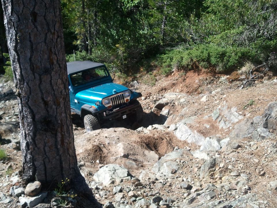 Teal Jeep Wrangler navigating a rocky off-road trail