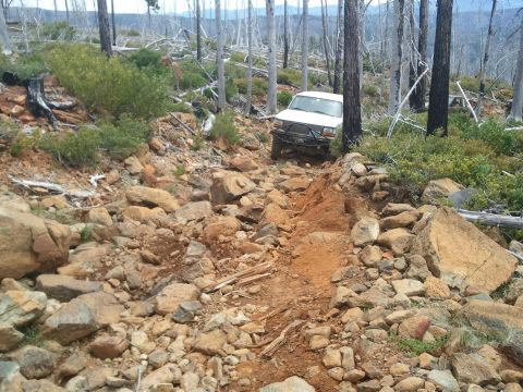 1994 Ford Bronco - White 1994 Ford Bronco tackles a challenging rocky trail in a wooded area.