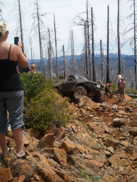 1994 Ford Bronco - Off-road vehicle attempts to climb a challenging rocky incline in a dry, wooded area.