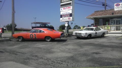 2000 Mercury Grand Marquis - The iconic General Lee and a police cruiser are parked side-by-side in a lot.
