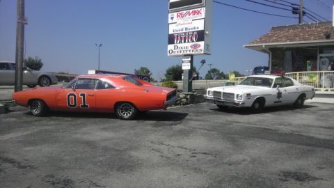 2000 Mercury Grand Marquis - Two cars, a classic Dodge Charger and a police car, are parked in a lot near a strip mall.