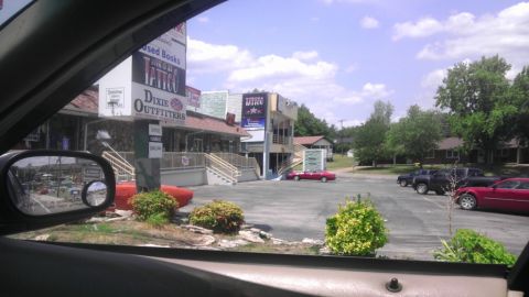 2000 Mercury Grand Marquis - A red sedan is parked in a lot outside of Dixie Outfitters and other businesses.