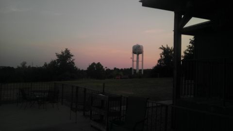 2000 Mercury Grand Marquis - A water tower stands tall in a rural landscape as the sun sets, casting a pink hue across the sky.