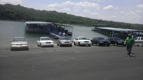 2000 Mercury Grand Marquis - A group of sedans are parked near a lake with docks and a wooded hillside.