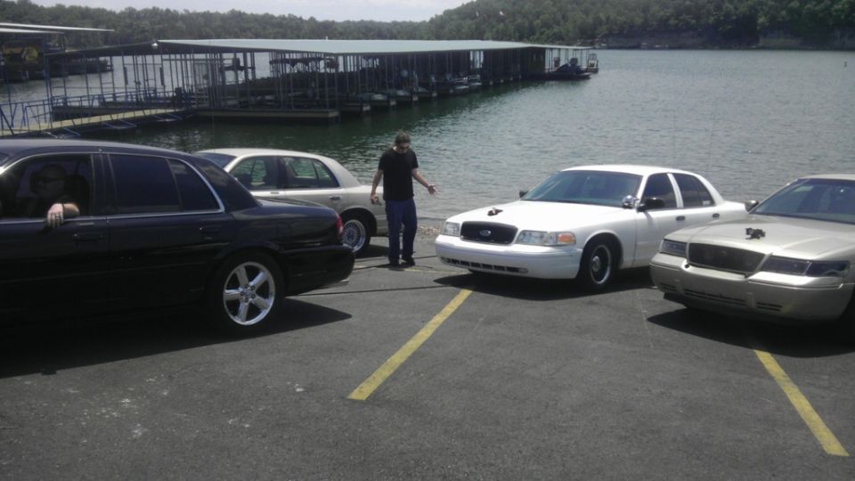 Three Ford Crown Victoria police cars parked by a lake with docks