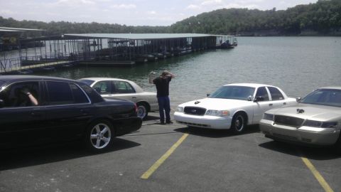 2000 Mercury Grand Marquis - Several sedans are parked near a lake with docks, with a person standing between two of them.