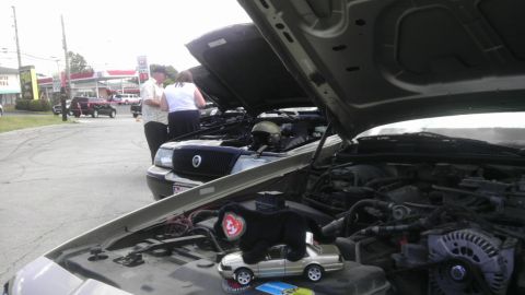 2000 Mercury Grand Marquis - Multiple vehicles are displayed with their hoods open, revealing their engines to onlookers.