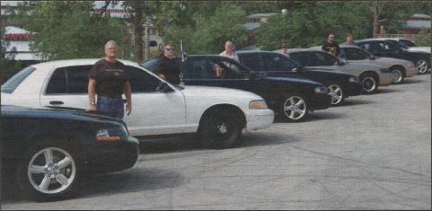2000 Mercury Grand Marquis - A group of police interceptor sedans are lined up, with several individuals standing near the vehicles.