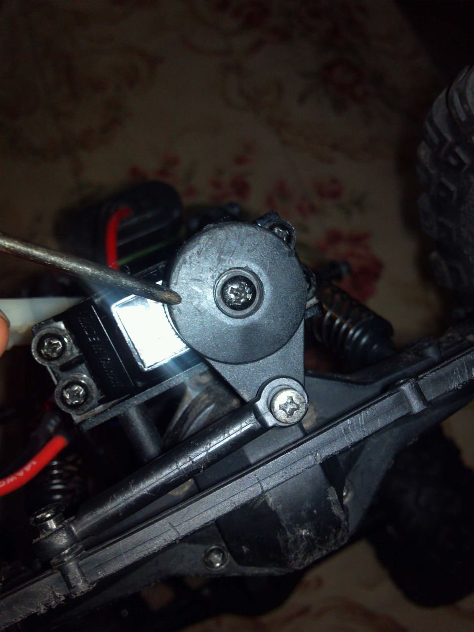 Black plastic servo horn on a remote control car chassis, being adjusted with a screwdriver