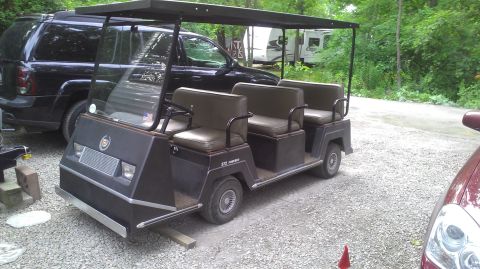 1991 Chevrolet Cheyenne - A six-seater golf cart is parked outdoors next to a black SUV and a red car.