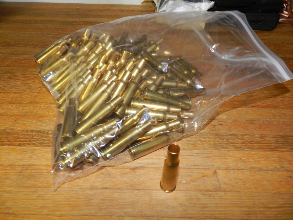 Bag of brass shell casings on a wooden surface, with one casing outside the bag