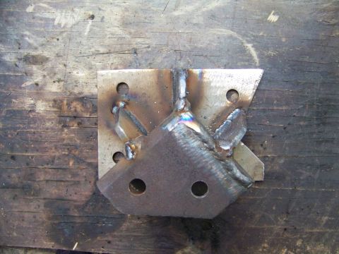 1985 Ford Bronco - A custom-fabricated metal bracket, likely for automotive modification, sits on a weathered wooden workbench.