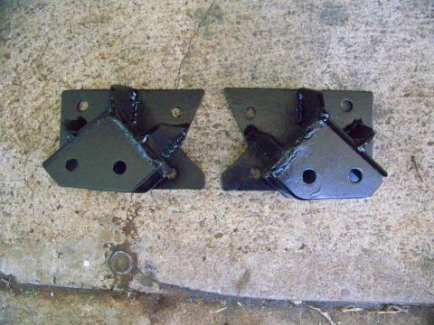 1985 Ford Bronco - Two black metal brackets, likely for vehicle modification, are shown on a concrete surface.