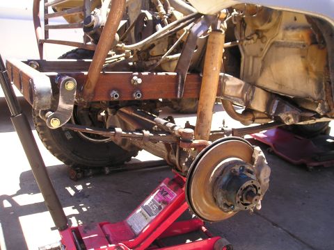 1987 Suzuki Samurai - Close-up view of a vehicle's rear suspension and axle, supported by a red hydraulic jack.