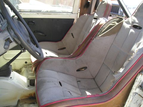 1987 Suzuki Samurai - The interior of a vehicle shows two worn racing seats and a steering wheel, with visible damage to the upholstery.