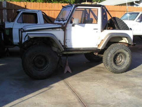 1987 Suzuki Samurai - Modified 1987 Suzuki Samurai on jack stands, with a partial view of another vehicle in the background.
