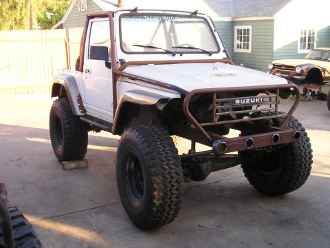 1987 Suzuki Samurai - Modified 1987 Suzuki Samurai with off-road tires and a custom roll cage sits in a driveway.