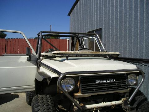1987 Suzuki Samurai - The front of a white 1987 Suzuki Samurai is visible with its driver's door open and a custom roll cage installed.
