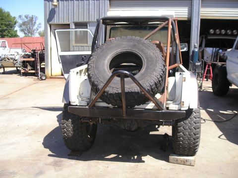 1987 Suzuki Samurai - A modified 1987 Suzuki Samurai is parked in a workshop with its rear end visible, spare tire, and custom roll cage visible.