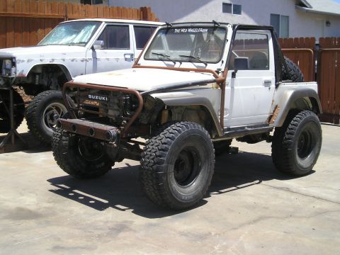 1987 Suzuki Samurai - Modified white Suzuki Samurai, possibly a 1987 model, sits in a driveway with a second vehicle in the background.