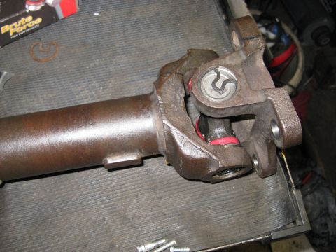 1994 Ford Bronco - A driveshaft universal joint with visible red seals and a retaining clip is shown on a workbench.